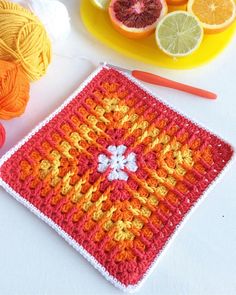 an orange and yellow crochet square next to some fruit