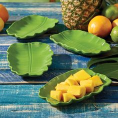 pineapple slices and oranges on green leaf shaped plates with fruit in the background