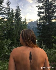 a person with a tattoo on their back standing in the woods looking at mountains and trees