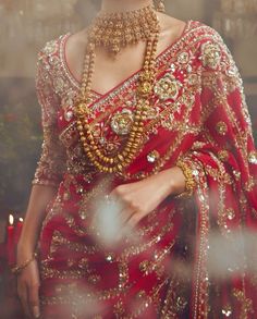 a woman in a red sari with gold jewelry on her neck and hands behind her back