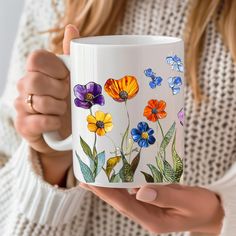 a woman holding a coffee mug with colorful flowers painted on the front and sides of it