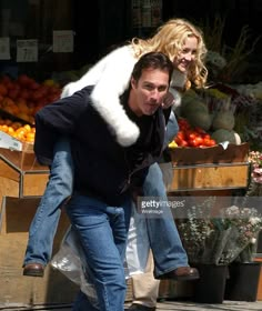 a man carrying a woman on his back in front of a fruit stand stock photo