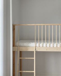 a wooden bunk bed sitting next to a white wall in a room with two ladders