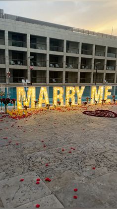 a large neon sign that says marry me in front of a building with rose petals on the ground