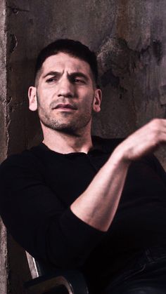 a man sitting in a chair with his arms crossed and looking at the camera while wearing a black shirt