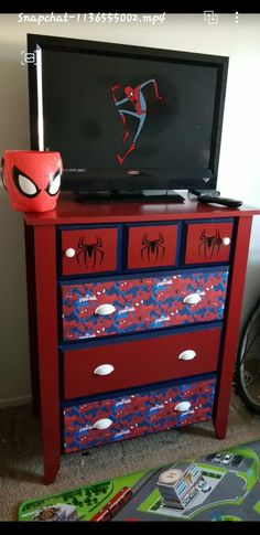 a red dresser with spiderman decals on the drawers and a television sitting on top