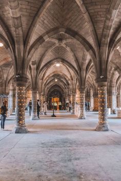 people are walking through an old building with columns and lights on the ceiling in front of them