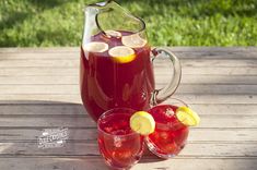 pitcher and glasses filled with red liquid sitting on a wooden table