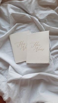 two pieces of paper with writing on them sitting on a bed covered in white sheets