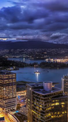 an aerial view of the city at night with lights on and water in the background