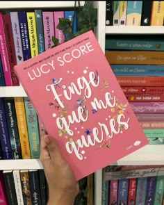 a person holding up a pink book in front of a bookshelf