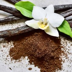 a white flower on top of some brown powder and cinnamon sticks with green leaves around it