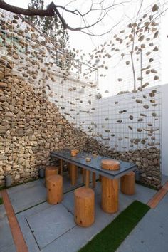 an outdoor table and stools in front of a wall made out of wood logs