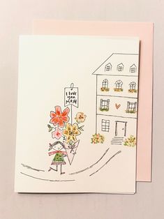 a greeting card with a drawing of a house and flowers on the front, along with a pink envelope that says i love you