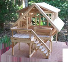 a wooden dollhouse with stairs to the upper floor and second story on top, in front of some trees