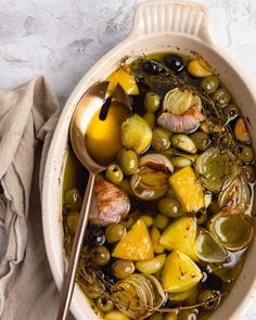 a bowl filled with olives, lemon and other vegetables next to a spoon on top of a cloth