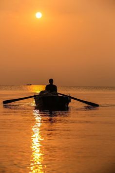 a man in a row boat on the water with the sun setting over the horizon