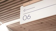 a white sign hanging from the side of a wooden ceiling next to a window with blinds on it