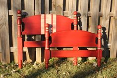 a red wooden bed frame sitting in the grass next to a fence and wood slats