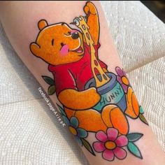 a winnie the pooh tattoo with flowers on her leg and an orange bear holding a honey pot