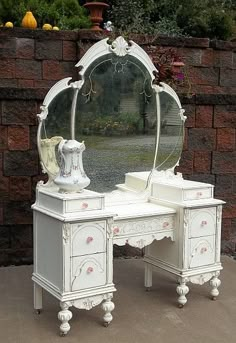 an antique white vanity with mirror and stool in front of a brick wall on the sidewalk