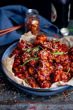 a bowl filled with meat covered in sauce and garnished with green onions next to chopsticks