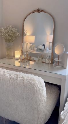 a white vanity with a mirror, stool and flowers in vases on the table