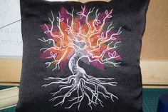 a black pillow with a colorful tree on the front and back side, sitting on a table