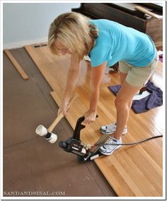 a woman in blue shirt holding a hammer on top of hard wood floor next to an electric drill