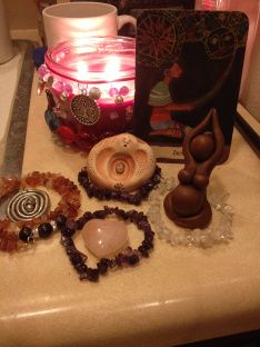 a table topped with lots of different types of jewelry next to a candle and book