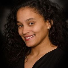 a woman with curly hair smiling at the camera in front of a black background,