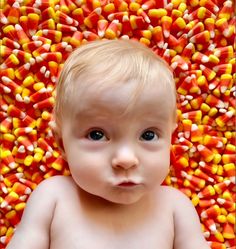 a baby is surrounded by candy corn in the shape of a head and shoulders, looking at the camera