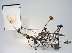 a sculpture made out of various objects on display in a white room with an easel next to it