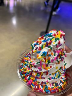 a hand holding a cup filled with white frosting and sprinkles on top of it