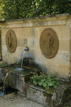 an outdoor fountain with statues on the sides and water running from it's sides