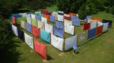 an aerial view of several rows of colorful clothes hanging in the grass with trees in the background