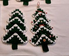 crocheted christmas tree ornaments hanging on a white tablecloth with red and green decorations