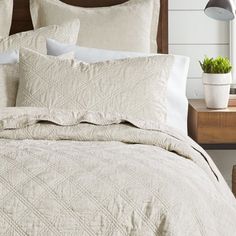 a bed with white linens and pillows on it, next to a night stand