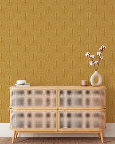 a white vase with flowers sitting on top of a wooden dresser next to a wall