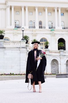 a woman wearing a graduation gown and holding a bouquet of flowers in front of the state capitol building