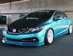 a blue honda civic with white rims parked in a parking lot next to a building