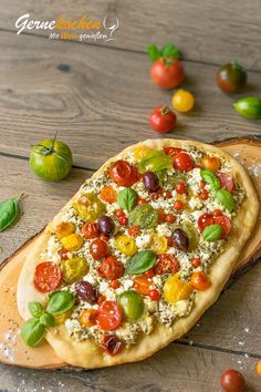 a pizza sitting on top of a wooden cutting board next to tomatoes and other vegetables