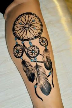 a woman's leg with a tattoo that has a dream catcher and beads on it