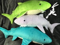 three stuffed sharks are laying on a black sheet with green and white ones in the middle