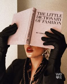 a woman holding up a book to her face while wearing black gloves and an earring