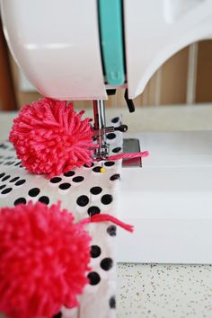 a sewing machine with pink pom - poms on it's handle and fabric