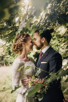 a bride and groom are standing under the tree branches in their wedding day attire, looking into each others eyes