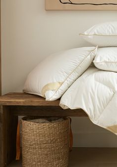 a bed with white pillows on top of it next to a wooden table and basket