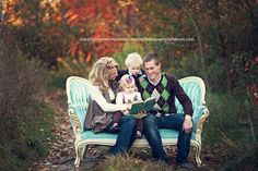 a family is sitting on a bench in the woods reading a book to their child