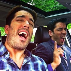 two men sitting in the back seat of a car with their mouths open and one man holding his hand up